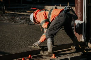 Pracownik budowlany wygładzający świeżą wylewkę betonową pacą na budowie.